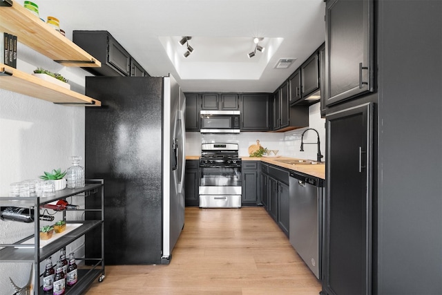 kitchen with light hardwood / wood-style flooring, a raised ceiling, butcher block counters, appliances with stainless steel finishes, and sink