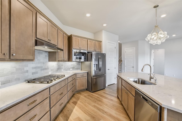 kitchen featuring stainless steel appliances, decorative backsplash, an inviting chandelier, light wood-type flooring, and sink