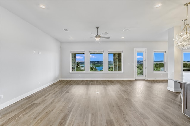 unfurnished living room with ceiling fan with notable chandelier, light hardwood / wood-style floors, and a wealth of natural light