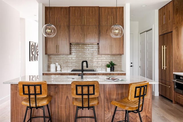 kitchen featuring oven, a kitchen bar, light wood-type flooring, decorative backsplash, and a kitchen island with sink