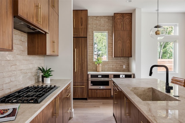 kitchen with sink, oven, hanging light fixtures, light stone countertops, and black gas stovetop