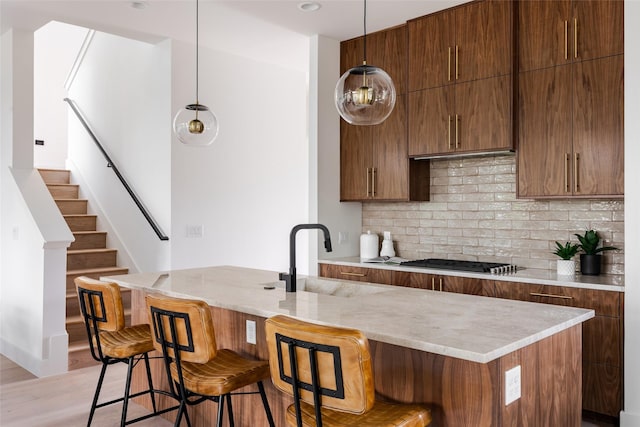 kitchen featuring sink, a kitchen breakfast bar, decorative backsplash, stainless steel gas stovetop, and pendant lighting