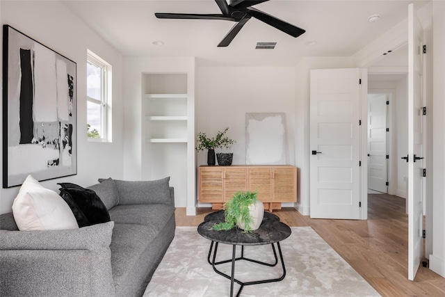 living room with ceiling fan, light hardwood / wood-style flooring, and built in shelves