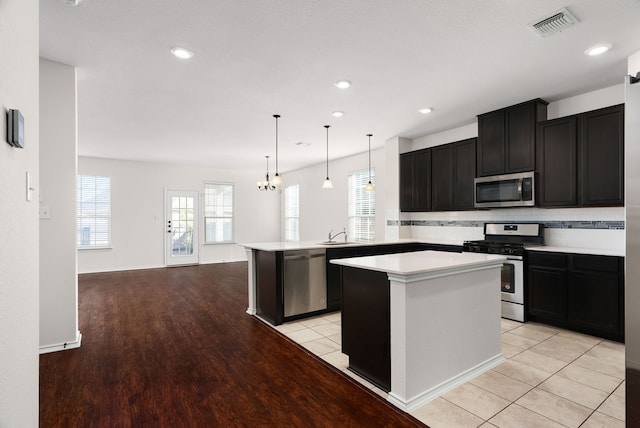 kitchen with a chandelier, pendant lighting, stainless steel appliances, decorative backsplash, and a kitchen island