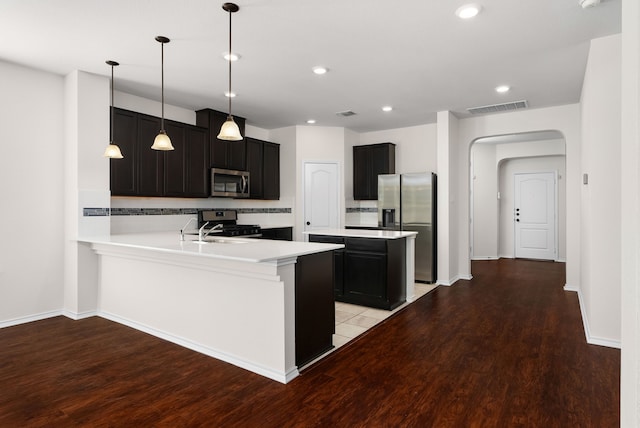 kitchen featuring stainless steel appliances, light wood-type flooring, kitchen peninsula, decorative backsplash, and hanging light fixtures