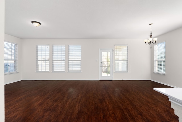 spare room with a notable chandelier and dark wood-type flooring