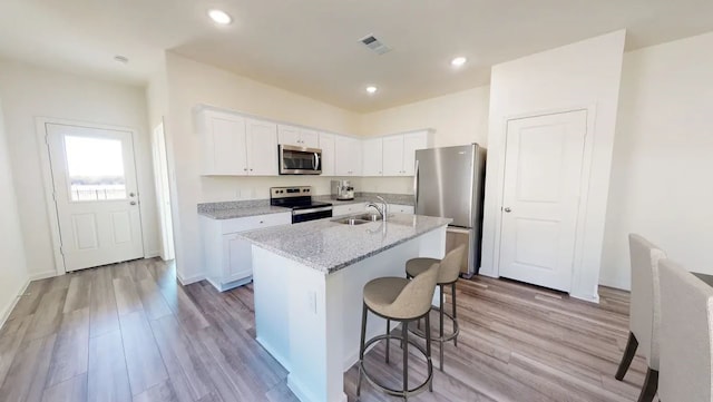 kitchen featuring light stone countertops, stainless steel appliances, light hardwood / wood-style floors, a kitchen island with sink, and white cabinetry