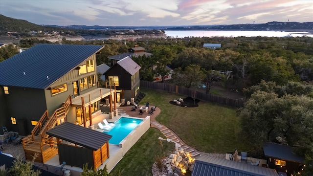 pool at dusk featuring a lawn, a patio area, a deck with water view, and a fire pit