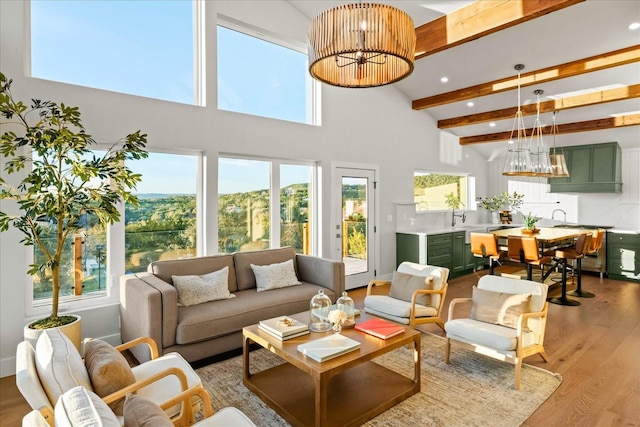 living room featuring a healthy amount of sunlight, a notable chandelier, light hardwood / wood-style floors, and beam ceiling