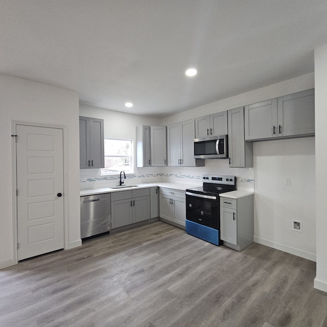 kitchen with stainless steel appliances, sink, light wood-type flooring, decorative backsplash, and gray cabinets