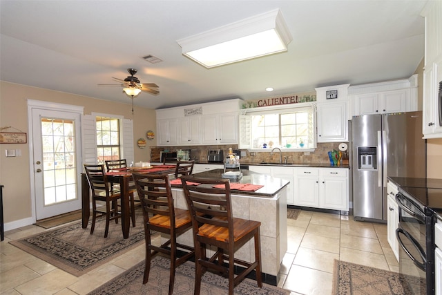 kitchen with light tile patterned floors, range with two ovens, stainless steel fridge, ceiling fan, and white cabinets