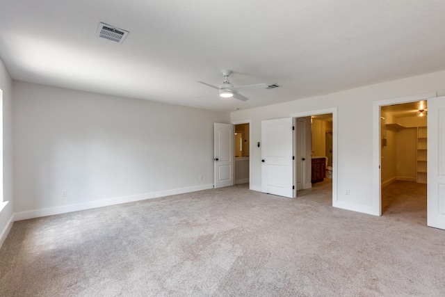 unfurnished bedroom with ceiling fan, a walk in closet, a closet, and light carpet