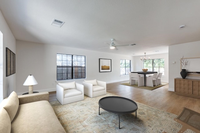 living room with ceiling fan with notable chandelier and light hardwood / wood-style floors