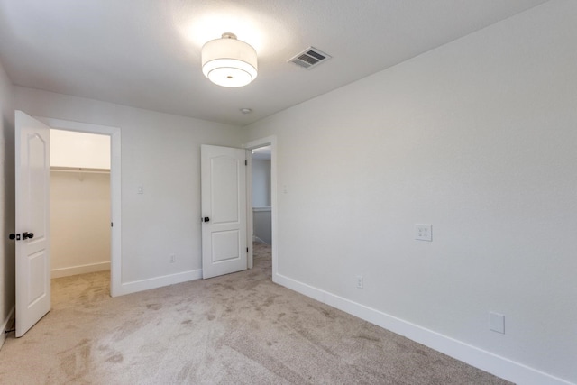 unfurnished bedroom featuring a walk in closet, light colored carpet, and a closet