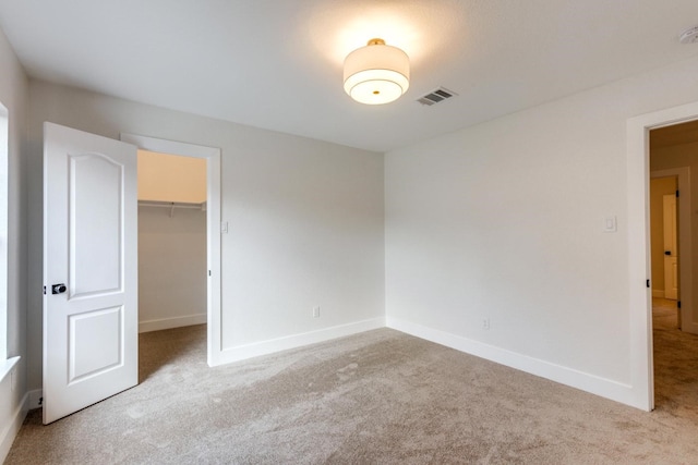 unfurnished bedroom with a walk in closet, a closet, and light colored carpet