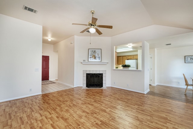 unfurnished living room featuring lofted ceiling, a tile fireplace, ceiling fan, and light hardwood / wood-style floors