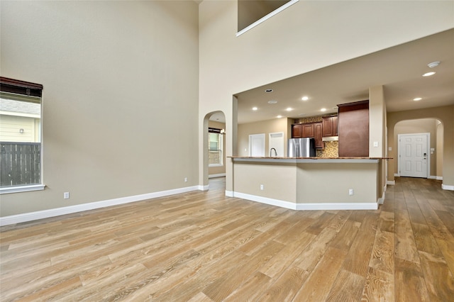 interior space featuring light wood-type flooring, kitchen peninsula, stainless steel fridge, decorative backsplash, and sink