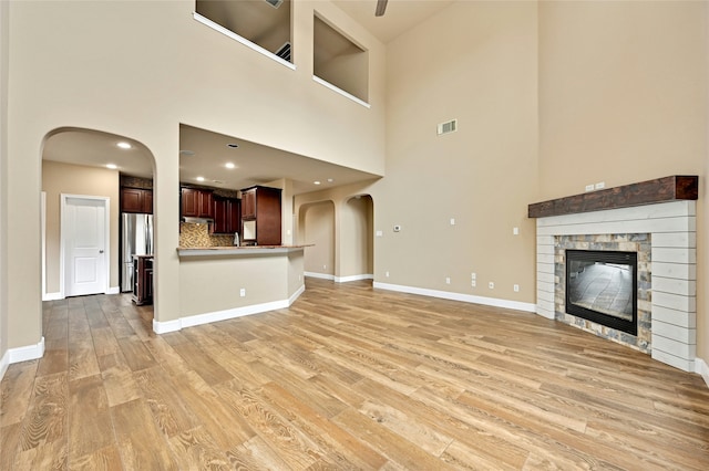 unfurnished living room with a towering ceiling, light wood-type flooring, and a stone fireplace