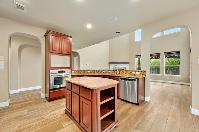 kitchen featuring appliances with stainless steel finishes, kitchen peninsula, light stone counters, a kitchen island, and light hardwood / wood-style flooring