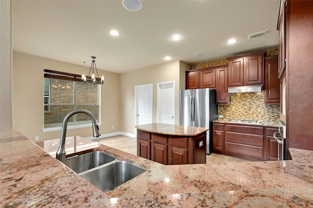 kitchen with light stone counters, hanging light fixtures, stainless steel appliances, an inviting chandelier, and sink