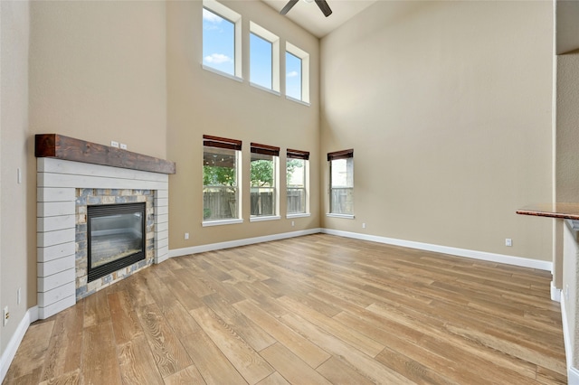 unfurnished living room featuring a high ceiling, a fireplace, ceiling fan, and light hardwood / wood-style floors