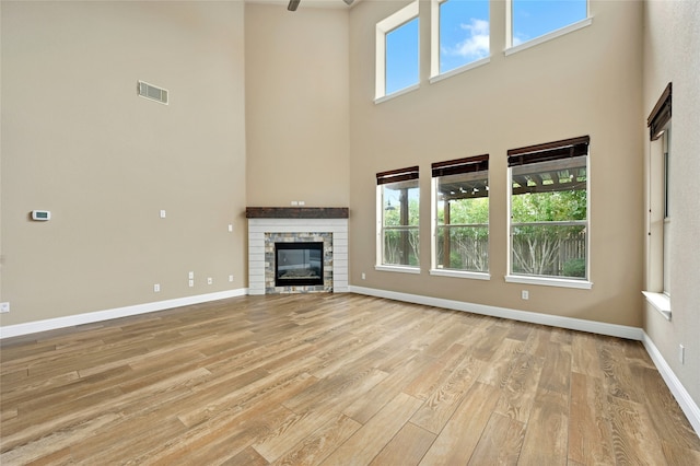 unfurnished living room with a high ceiling, light hardwood / wood-style floors, a wealth of natural light, and a stone fireplace