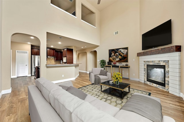 living room featuring a high ceiling, light hardwood / wood-style floors, and a stone fireplace