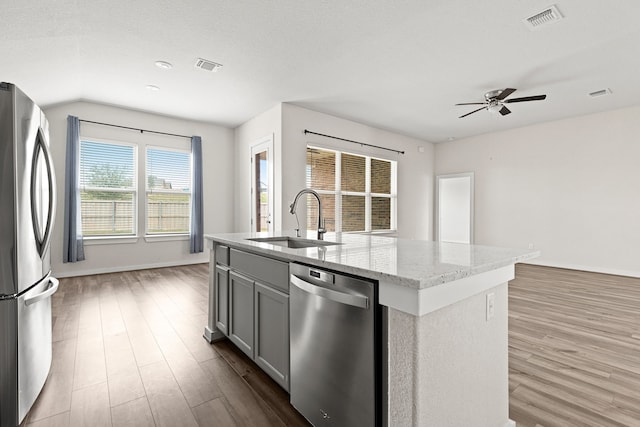 kitchen with sink, light stone counters, gray cabinets, a center island with sink, and appliances with stainless steel finishes