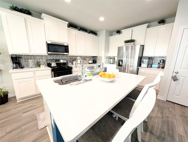 kitchen featuring stainless steel appliances, sink, white cabinetry, light wood-type flooring, and an island with sink