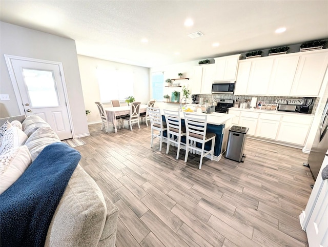 kitchen featuring stainless steel appliances, white cabinetry, a center island, a kitchen bar, and a healthy amount of sunlight