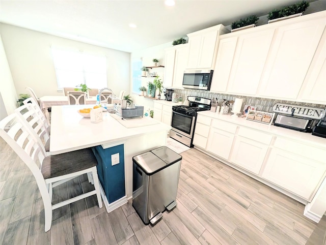 kitchen with white cabinetry, light hardwood / wood-style floors, a breakfast bar area, a center island with sink, and appliances with stainless steel finishes