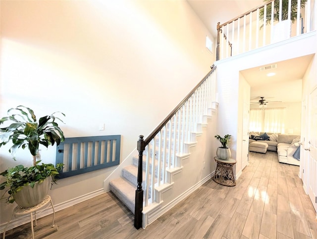 stairs with a high ceiling, ceiling fan, and wood-type flooring