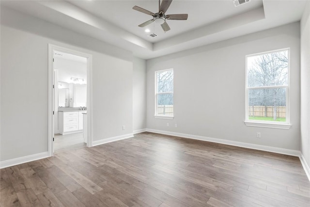 empty room featuring hardwood / wood-style flooring, ceiling fan, and a tray ceiling