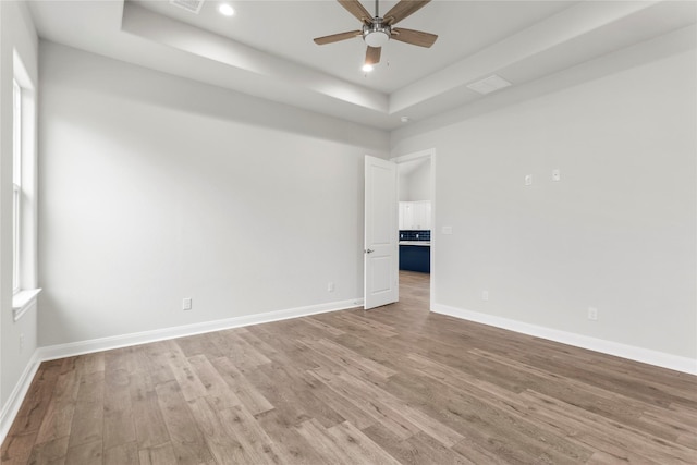 spare room with ceiling fan, light wood-type flooring, and a tray ceiling