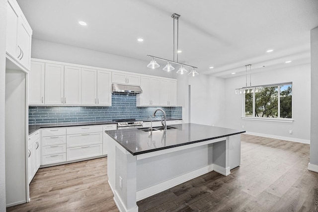 kitchen featuring hanging light fixtures, stainless steel range with electric cooktop, a kitchen island with sink, white cabinets, and sink