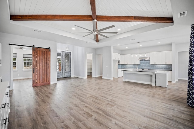 unfurnished living room featuring light hardwood / wood-style floors, a barn door, wooden ceiling, ceiling fan, and beamed ceiling