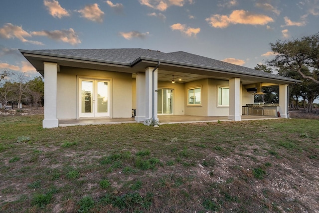 back house at dusk with french doors, an outdoor kitchen, a patio, and a yard