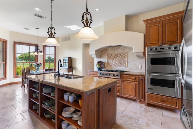 kitchen featuring stainless steel appliances, an island with sink, a notable chandelier, sink, and decorative light fixtures