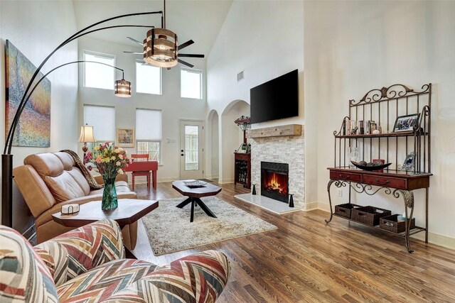 living room with a towering ceiling, a stone fireplace, ceiling fan, and hardwood / wood-style floors