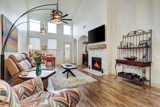living area with wood finished floors, a fireplace, plenty of natural light, arched walkways, and a ceiling fan