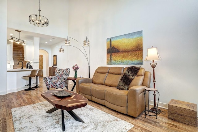 living room with wood finished floors, baseboards, arched walkways, a towering ceiling, and a notable chandelier