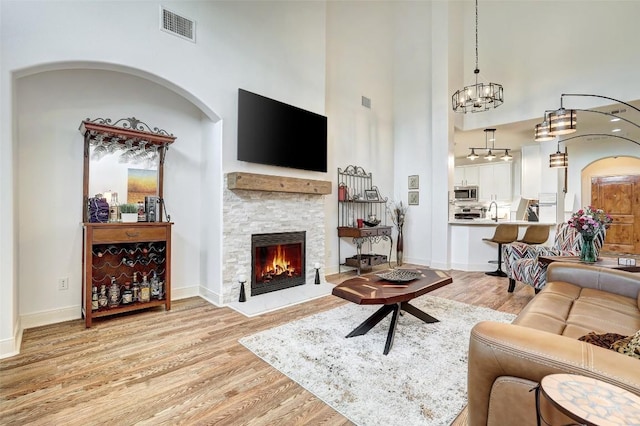 living room with visible vents, baseboards, a fireplace, a high ceiling, and wood finished floors