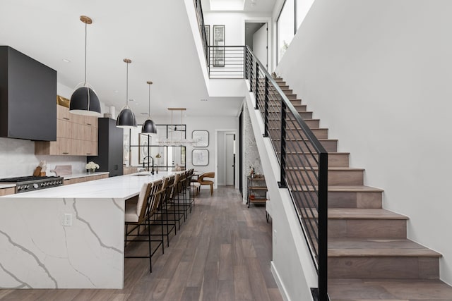 kitchen featuring a center island with sink, light stone countertops, a breakfast bar, light brown cabinets, and decorative light fixtures