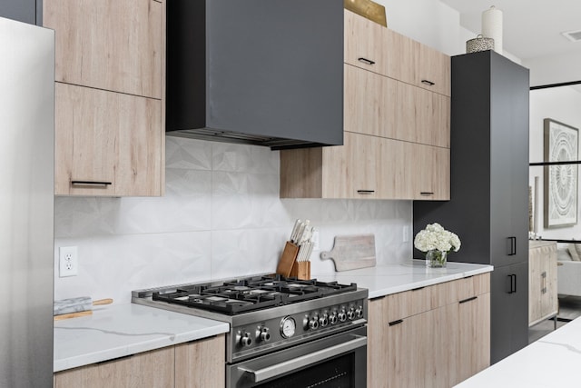 kitchen featuring light brown cabinetry, high end stove, light stone countertops, and tasteful backsplash