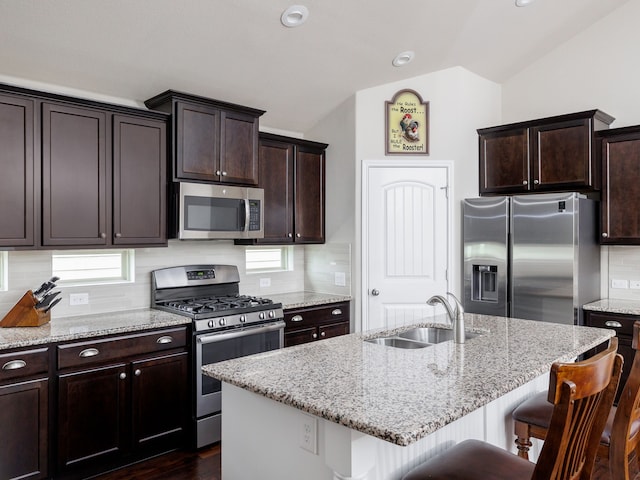 kitchen featuring sink, lofted ceiling, a kitchen breakfast bar, an island with sink, and appliances with stainless steel finishes