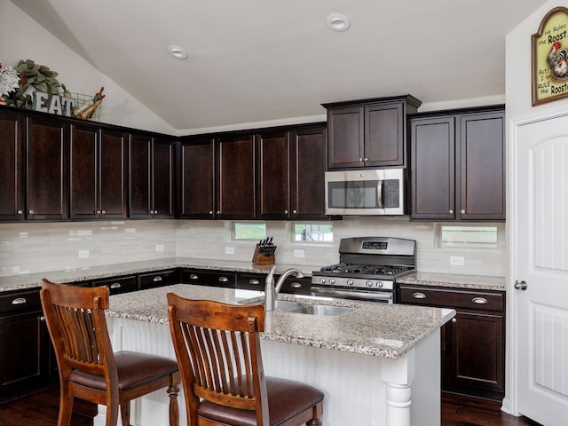 kitchen with stainless steel appliances, a kitchen island with sink, and light stone counters