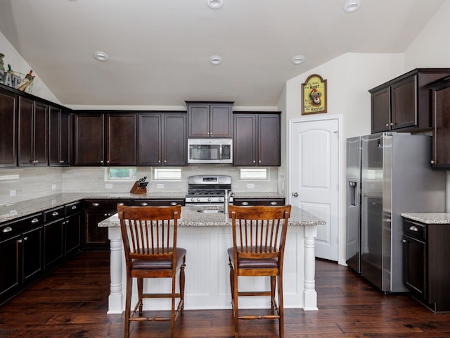 kitchen featuring light stone countertops, a center island with sink, dark brown cabinetry, and appliances with stainless steel finishes