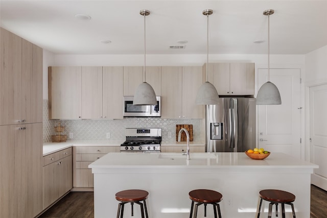 kitchen with stainless steel appliances, hanging light fixtures, and a center island with sink