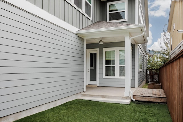 view of exterior entry featuring ceiling fan and a yard