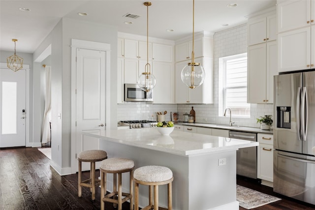 kitchen with a kitchen island, stainless steel appliances, white cabinets, and pendant lighting